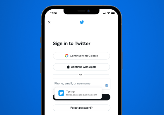 “Twitter로 로그인” 페이지가 표시되어 있는 확대된 iPhone, “전화, 이메일 또는 사용자 이름” 필드에 1Password Safari 확장 아이콘이 있고, 원 탭 로그인을 가능하게 하는 인라인 로그인 제안이 표시됨.